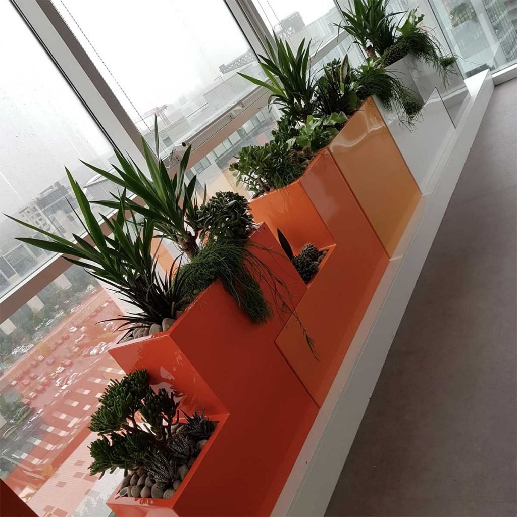 Orange and white gloss planters of varying heights with mixed live planting draped over the top to soften