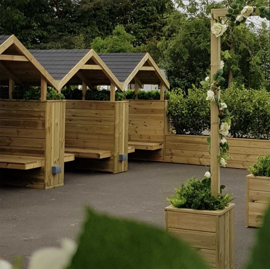 Bespoke booths, planters filled with greenery and archways wrapped with artificial foliage cream roses and ivy