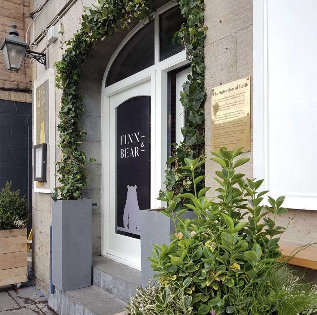 A foliage archway from two grey planters and wooden planters on wheels filled with plants for outdoor dining space