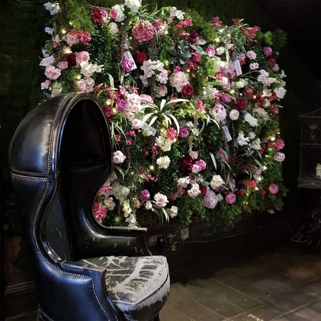 Chambord sponsored flower wall filled with artificial roses, hydrangea and leafy greenery behind a leather chair